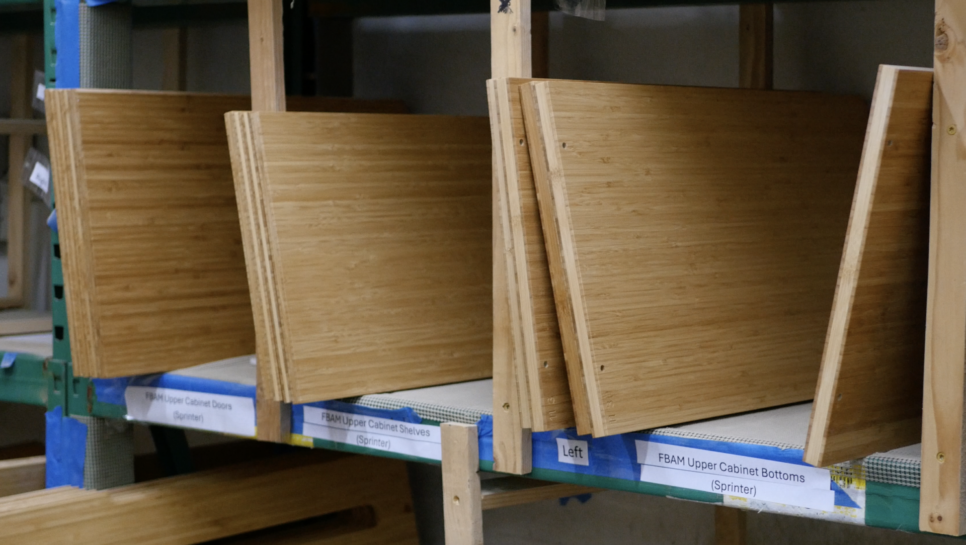 Wood cabinet doors propped on a warehouse shelf, labeled FBAM Upper Cabinet Doors (Sprinter) and Upper Cabinet Bottoms (Sprinter).